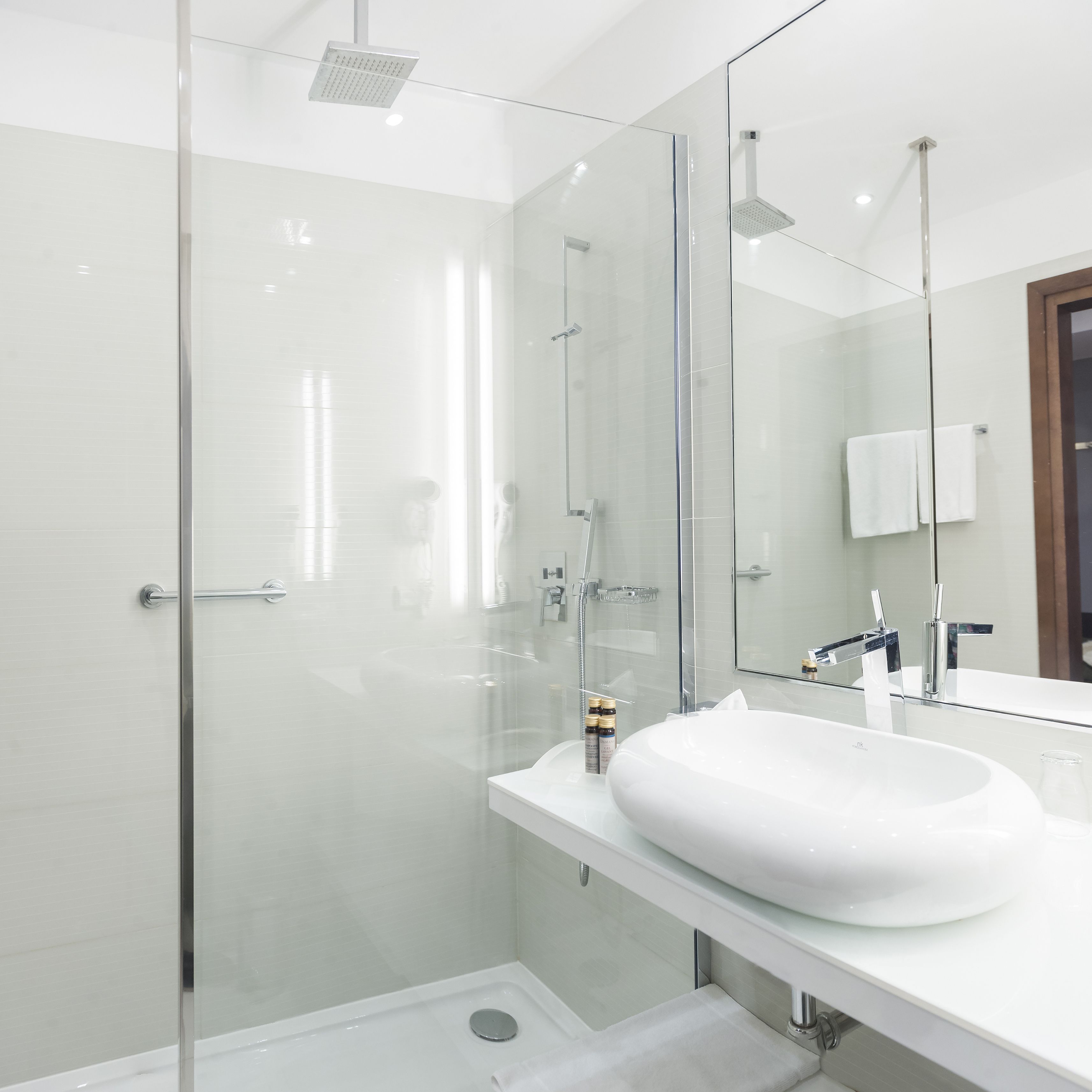 Un baño moderno con ducha de vidrio, un lavamanos blanco y un espejo grande.