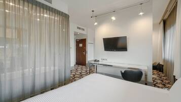 A hotel room with a bed, a desk, a chair, a television, and a window with curtains.