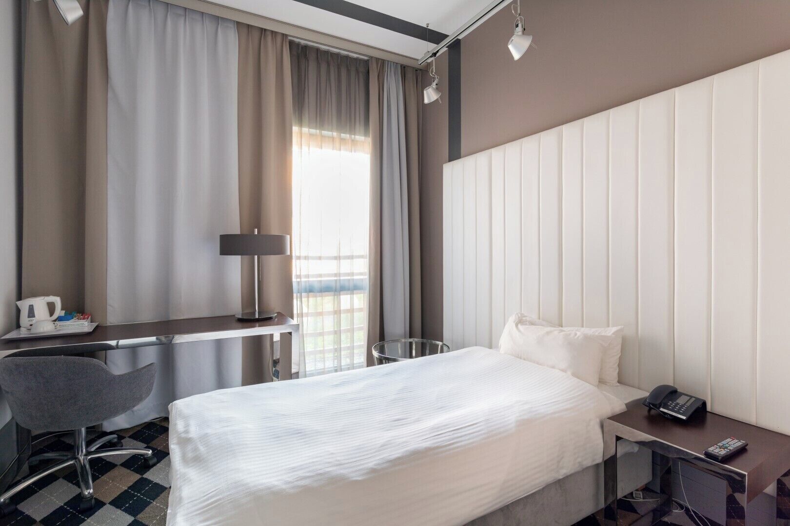 A hotel room with a bed, desk, chair, and a phone on the nightstand.