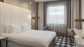 Ein Hotelzimmer mit einem großen Bett, einem Schreibtisch, einem Stuhl und einem Vorhangfenster.