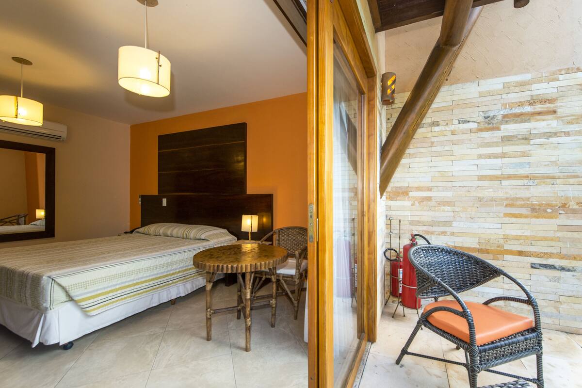 Een slaapkamer met een bed, nachtkastje, stoel en uitzicht op een bakstenen muur.