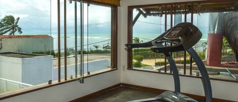 A gym with a treadmill and large windows overlooking the ocean.