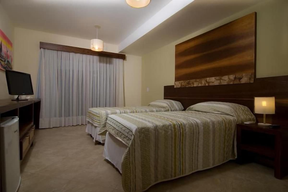 Une chambre d’hôtel avec deux lits, un bureau, une télévision et une fenêtre avec des rideaux.