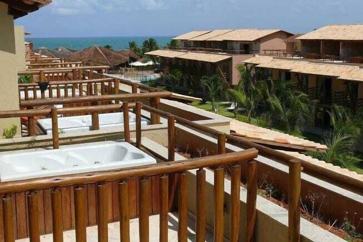 Een balkon van een resort met een houten hekwerk, een hottub en uitzicht op de oceaan en andere gebouwen van het resort.