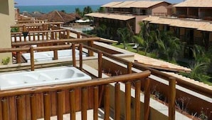 Balcón de un resort con barandilla de madera, bañera de hidromasaje y vista al océano y otros edificios del complejo.