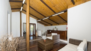 Una habitación amplia con techo alto, vigas de madera, mobiliario de mimbre y una cama blanca.