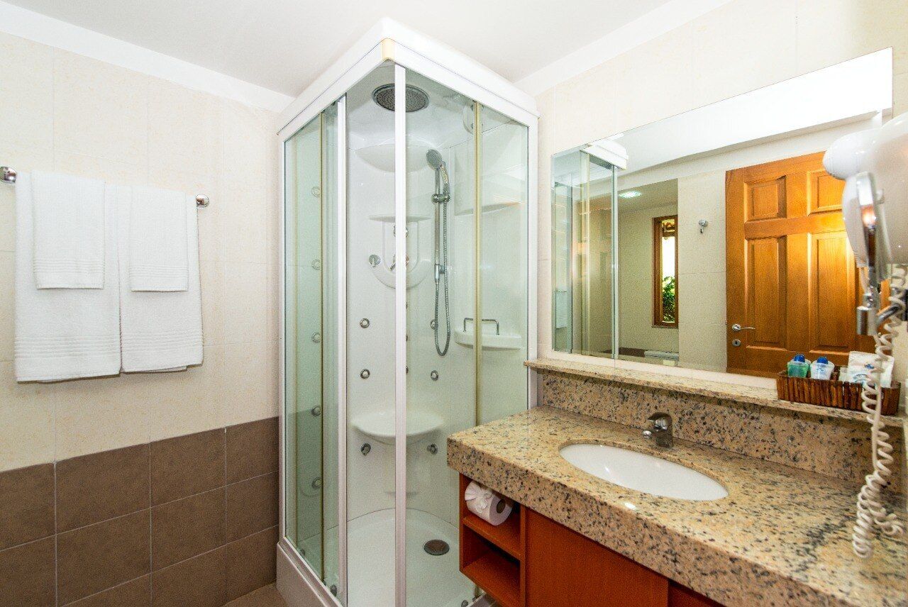Un baño moderno con ducha de vidrio, lavamanos con encimera de granito y espejo sobre el lavamanos.