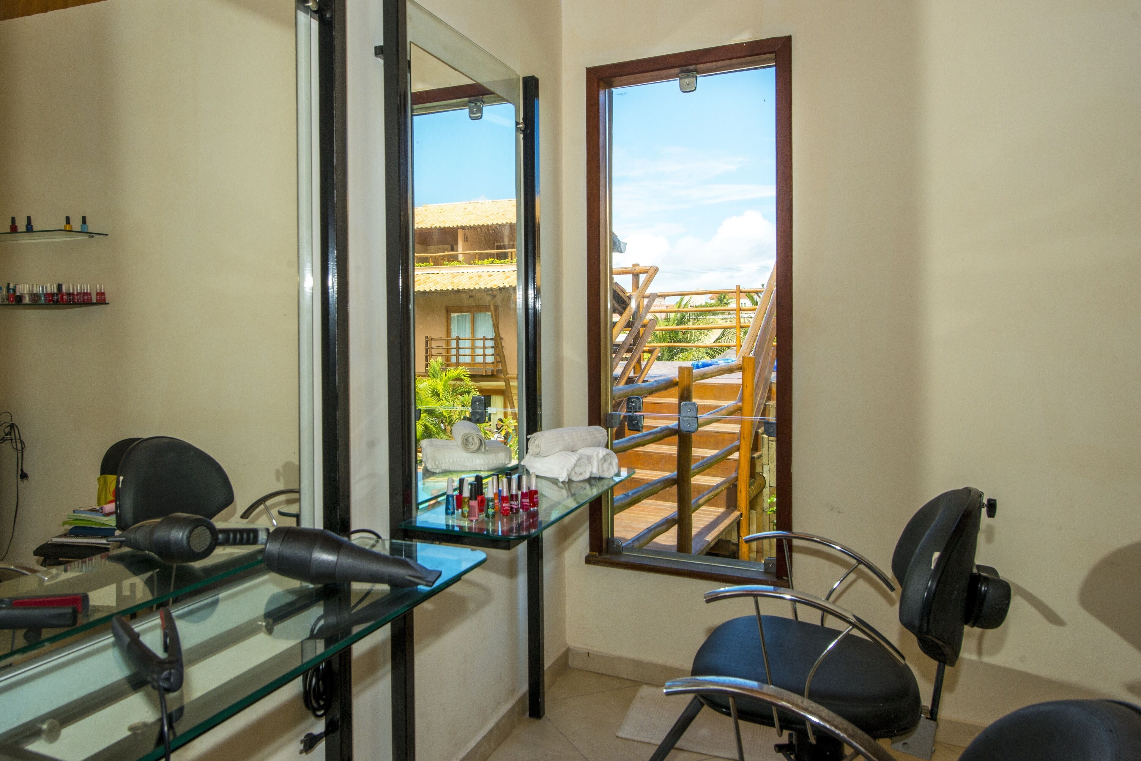 A room with a glass partition, a chair, a table with hair styling tools, and a window with a view of a balcony and outdoor area.