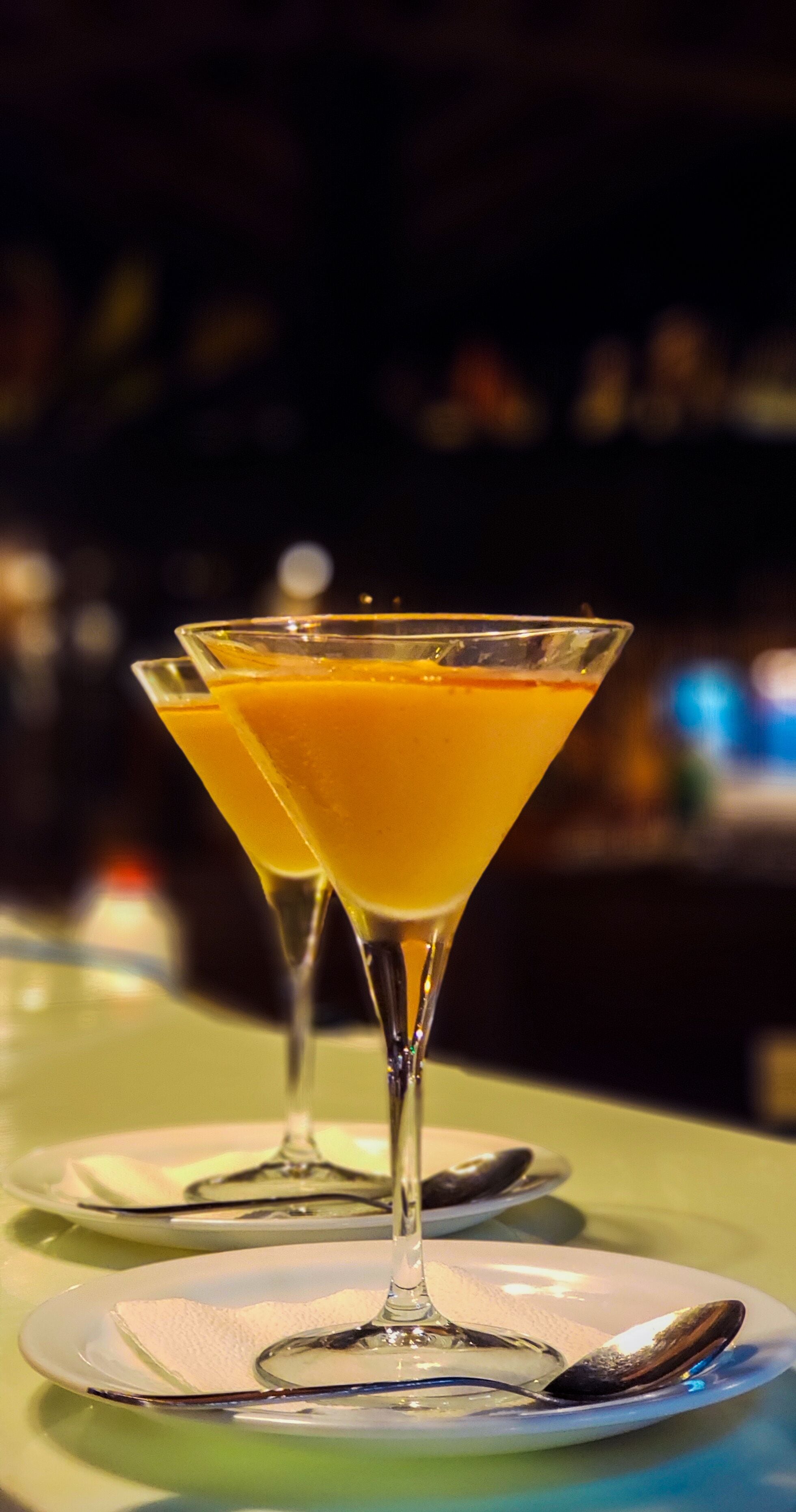 Due bicchieri da martini riempiti con una bevanda giallastra-arancione su un tavolo con superficie verde.