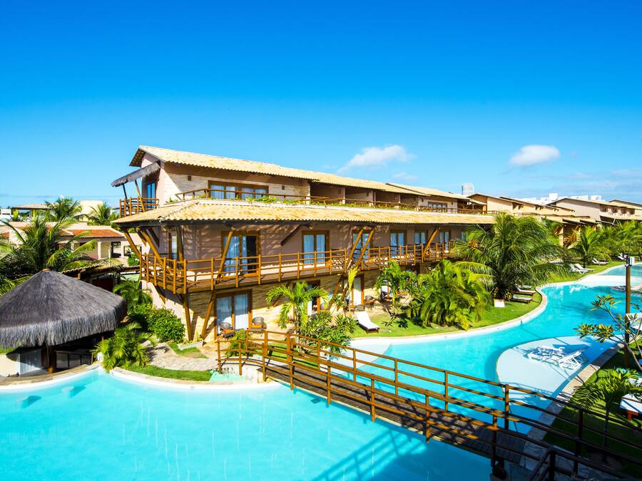 Um resort com uma grande piscina, vários quartos para hóspedes e exuberante paisagismo tropical.