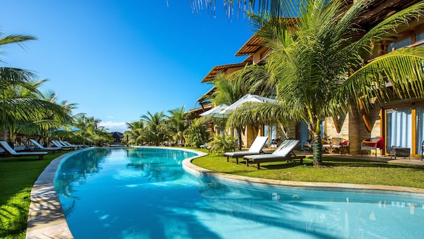 Una piscina con sillas de descanso y palmeras, rodeada de edificios de estilo tropical.