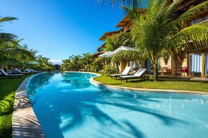 Una piscina con sillas de descanso y palmeras, rodeada de edificios de estilo tropical.