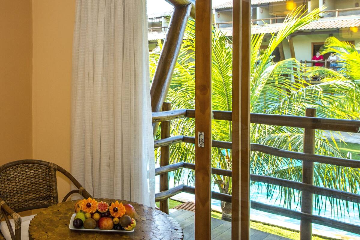 Een balkon met een houten hekwerk, een rieten stoel en een tafel met een fruitschaal.