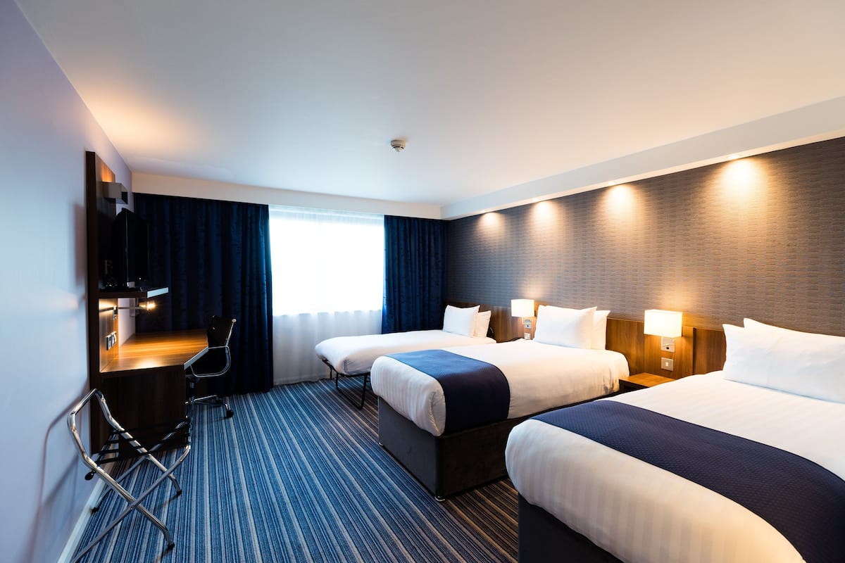 A hotel room with two beds, a desk, a chair, and a TV.
