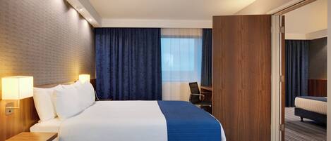 A hotel room with a large bed, a desk, a chair, a wardrobe, and a mirror.
