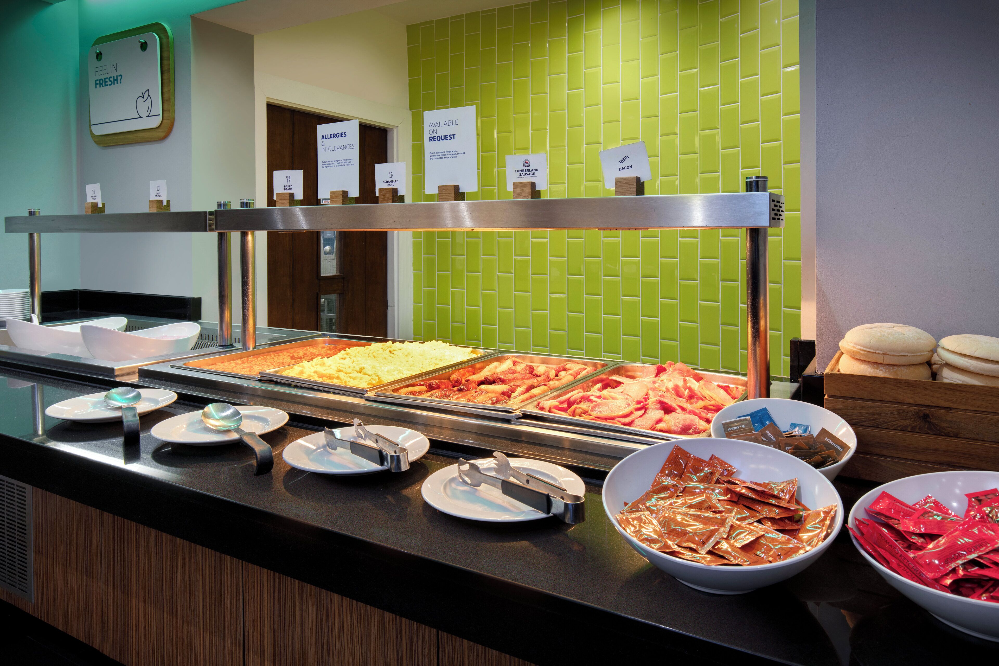 A buffet with various food options including baked beans, scrambled eggs, Cumberland sausage, bacon, and a selection of condiments.