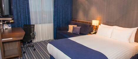 A hotel room with a large bed, a desk with a chair, a television, and a lamp.