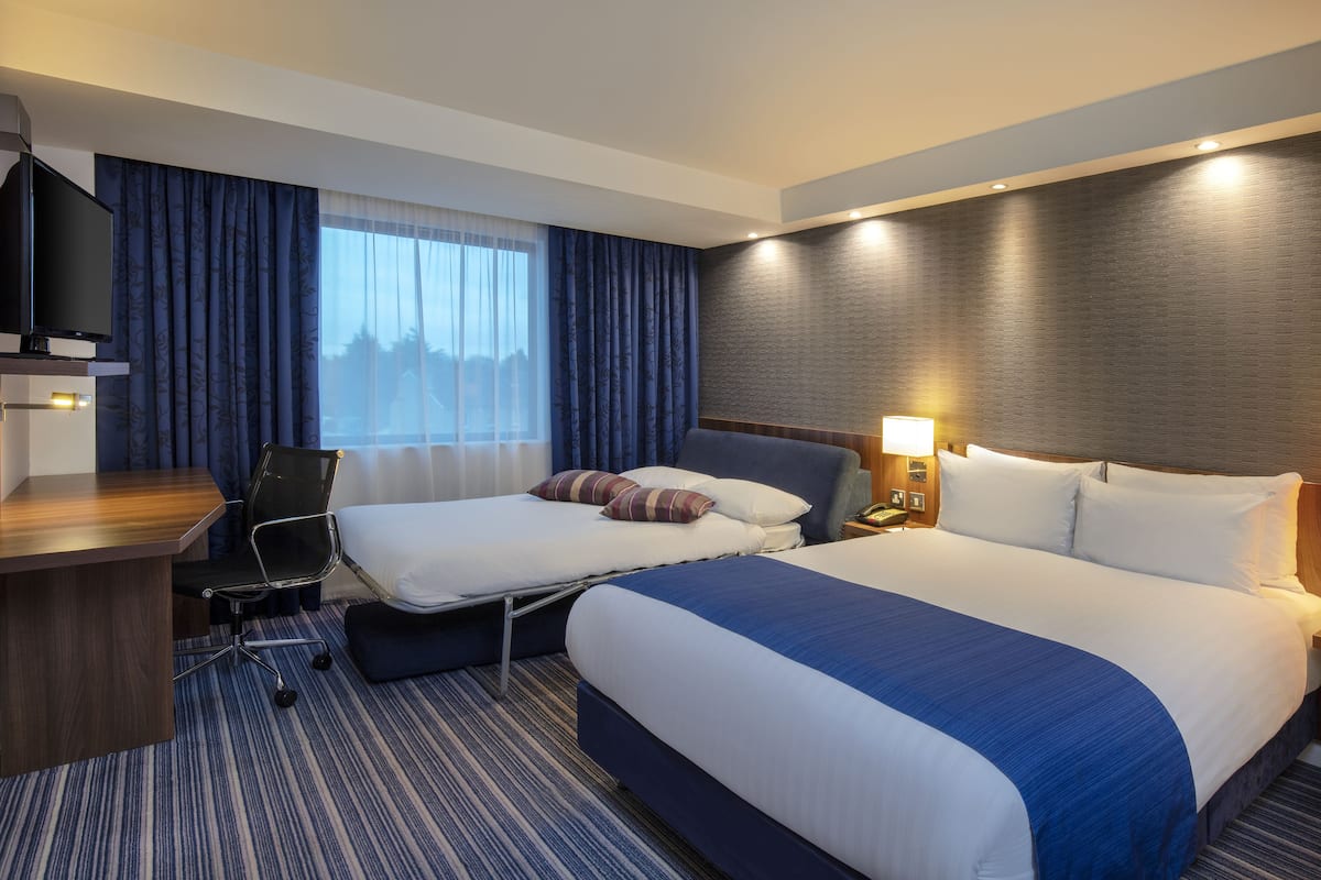 A hotel room with two beds, a desk, a chair, and a TV.
