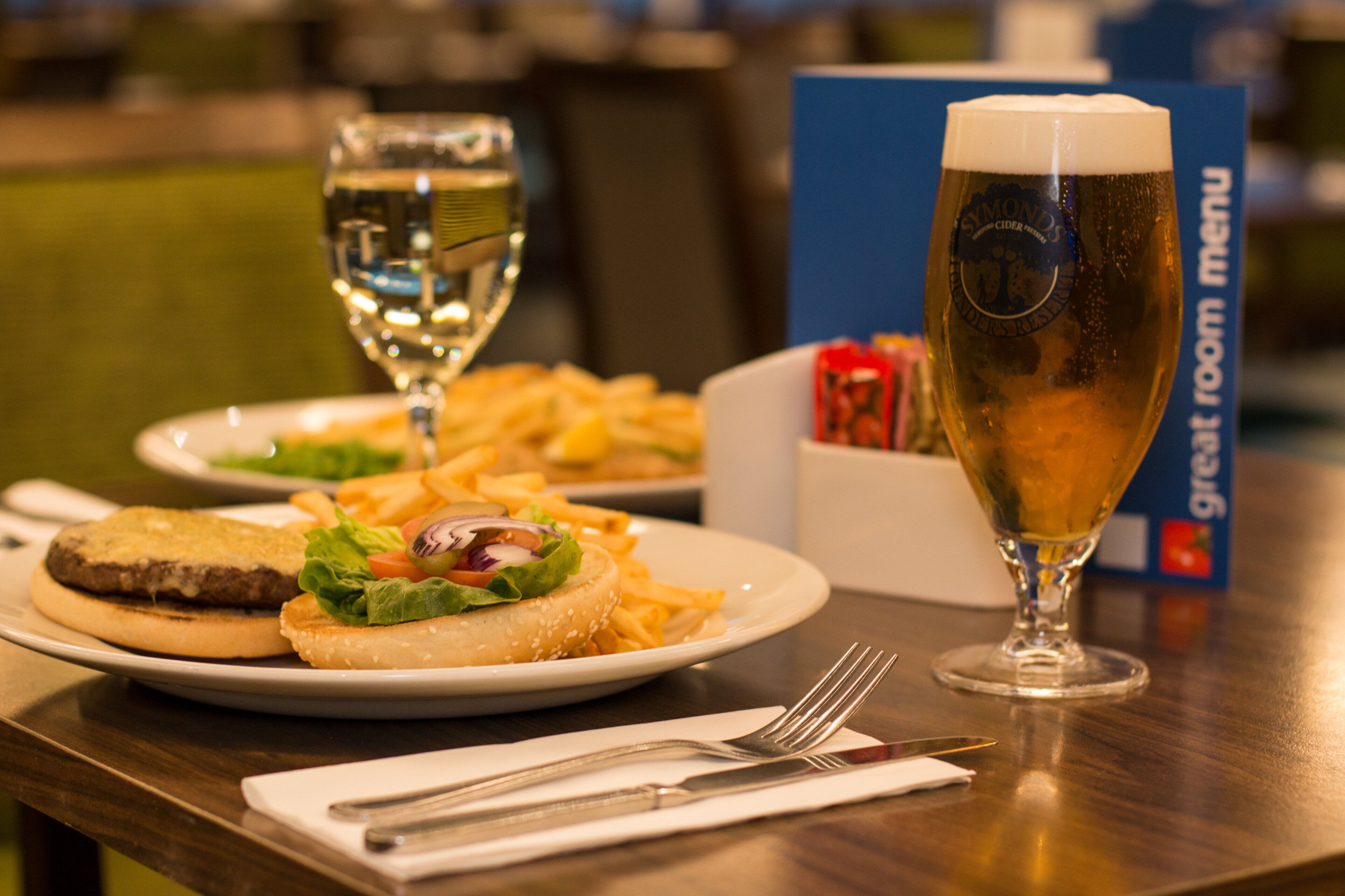 Un plato con una hamburguesa, papas fritas y una cerveza en una mesa con un menú y cubiertos.
