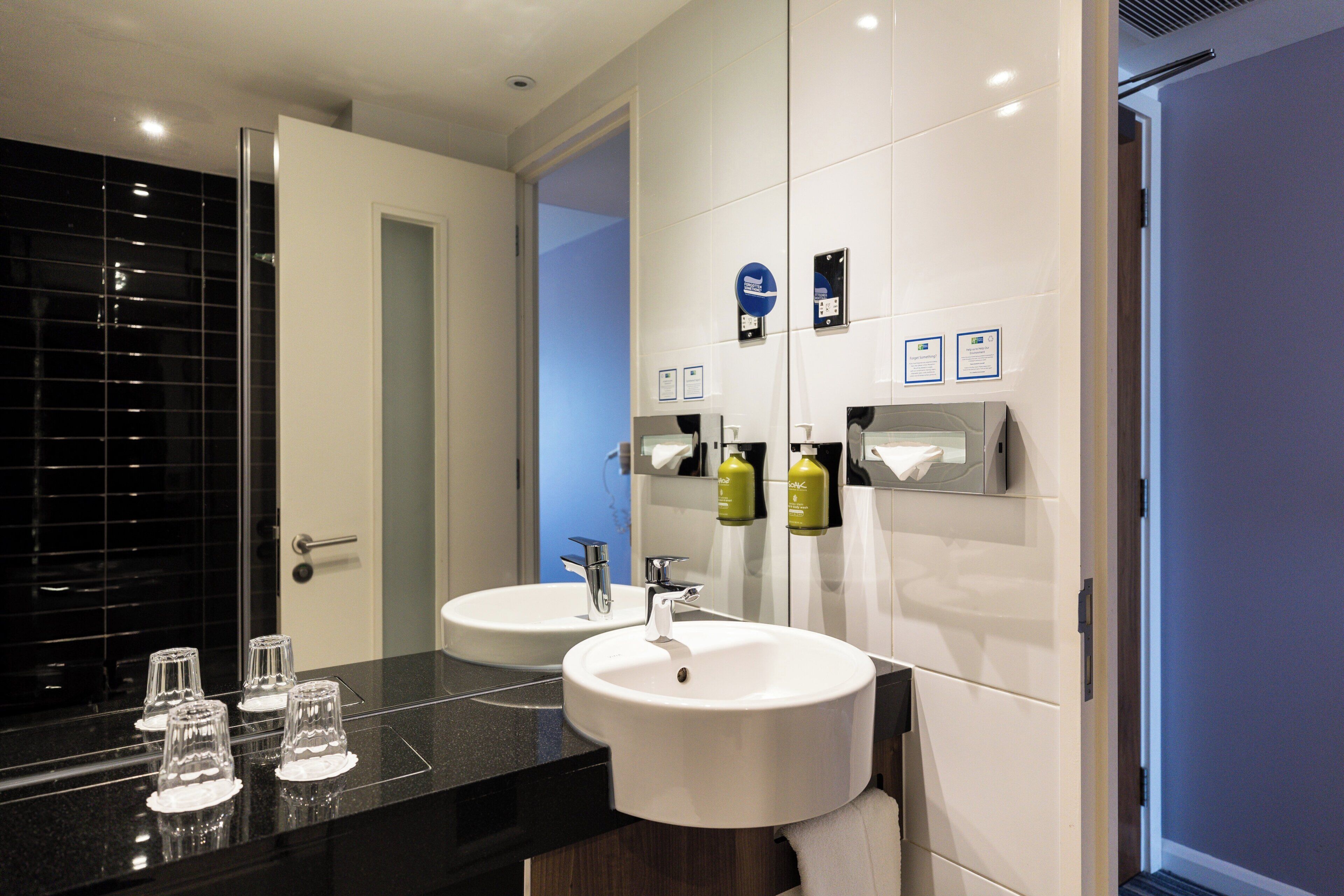 A modern bathroom with two sinks, a mirror, and a glass door leading to a shower area.