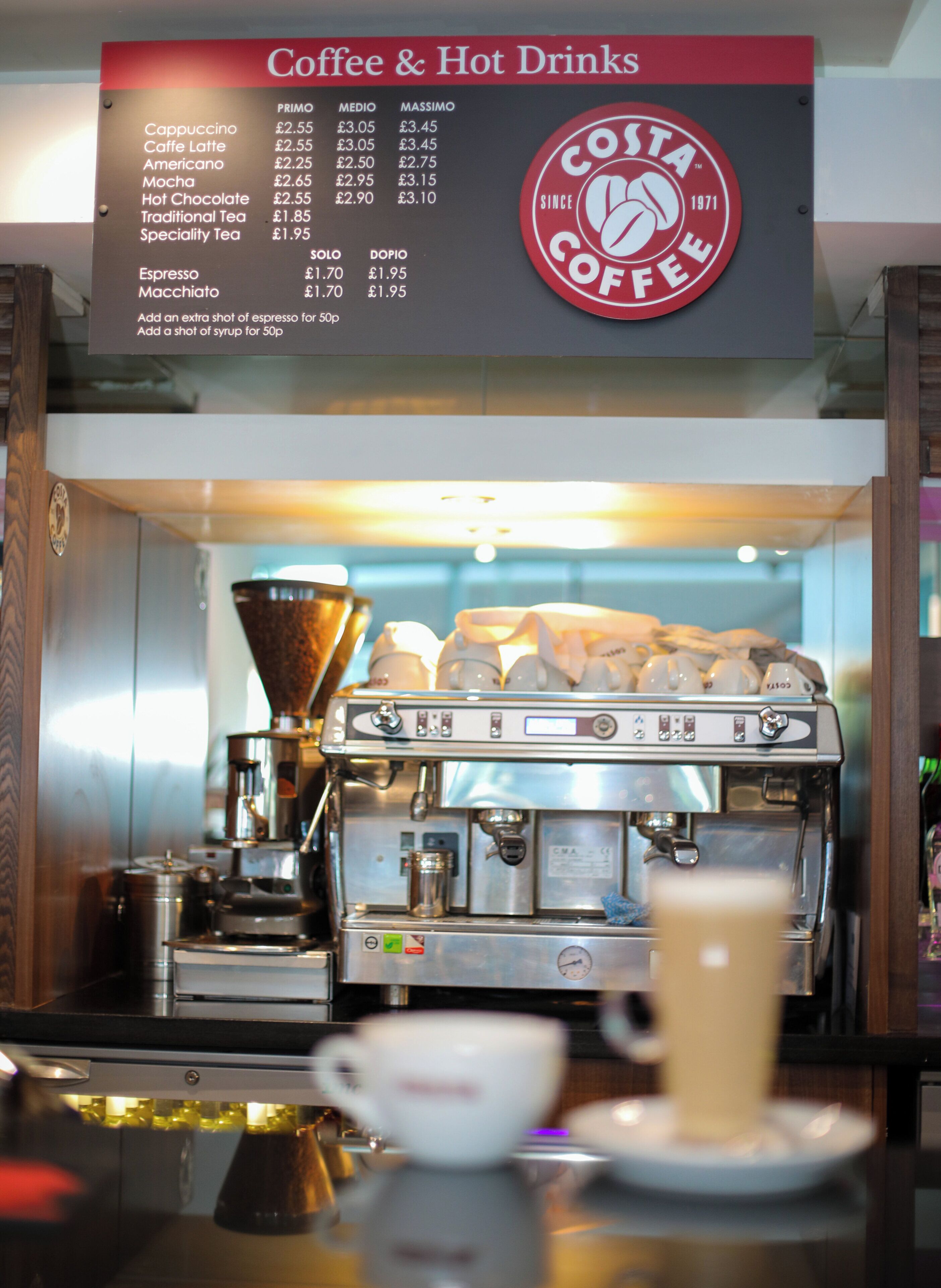 A coffee machine and a menu board for coffee and hot drinks at Costa Coffee.
