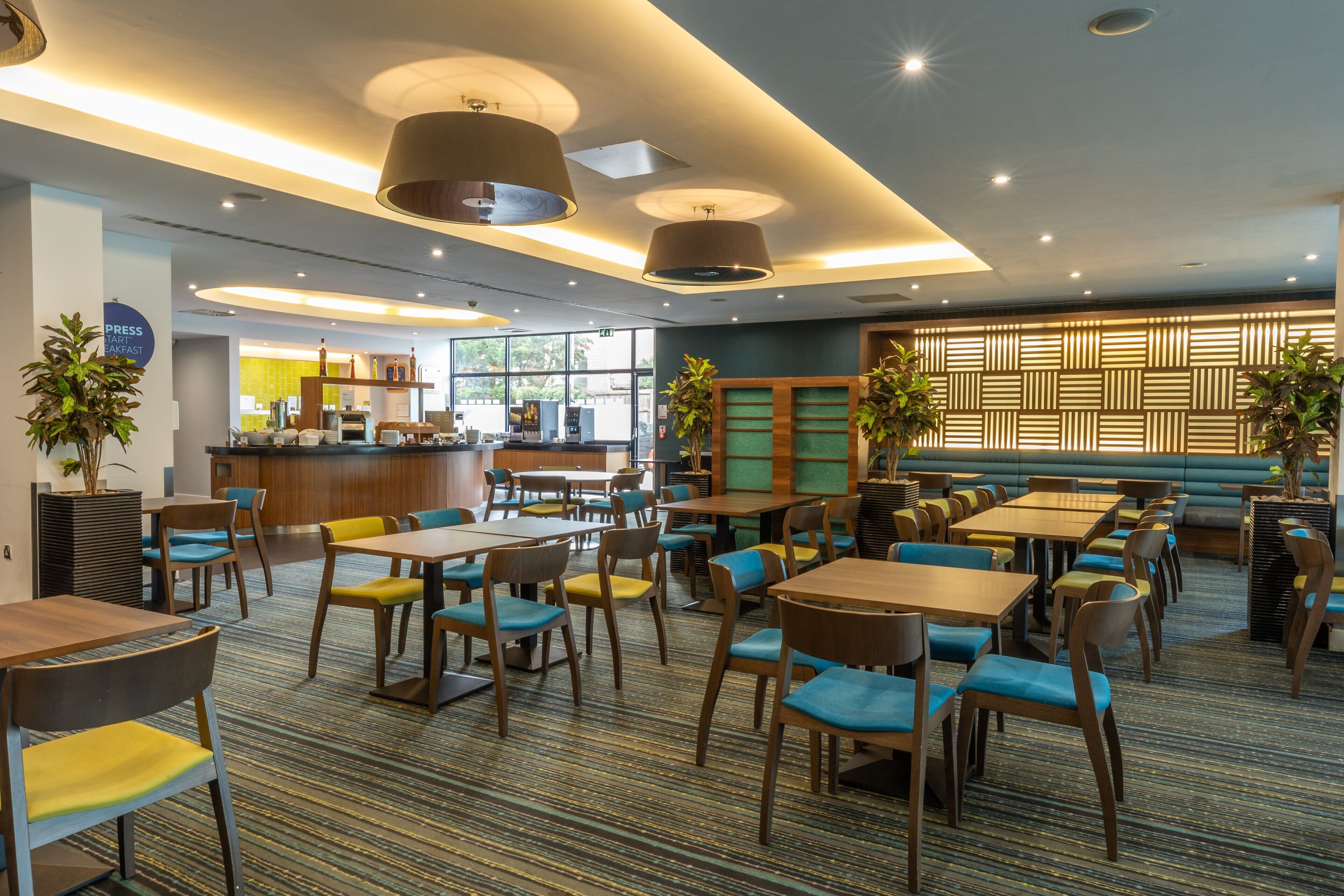 A modern restaurant with multiple seating areas, including tables and booths, and a bar in the background.