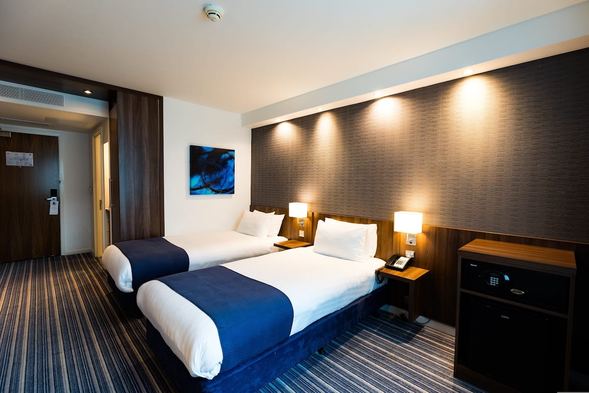 A hotel room with two beds, a desk, a lamp, and a minibar.