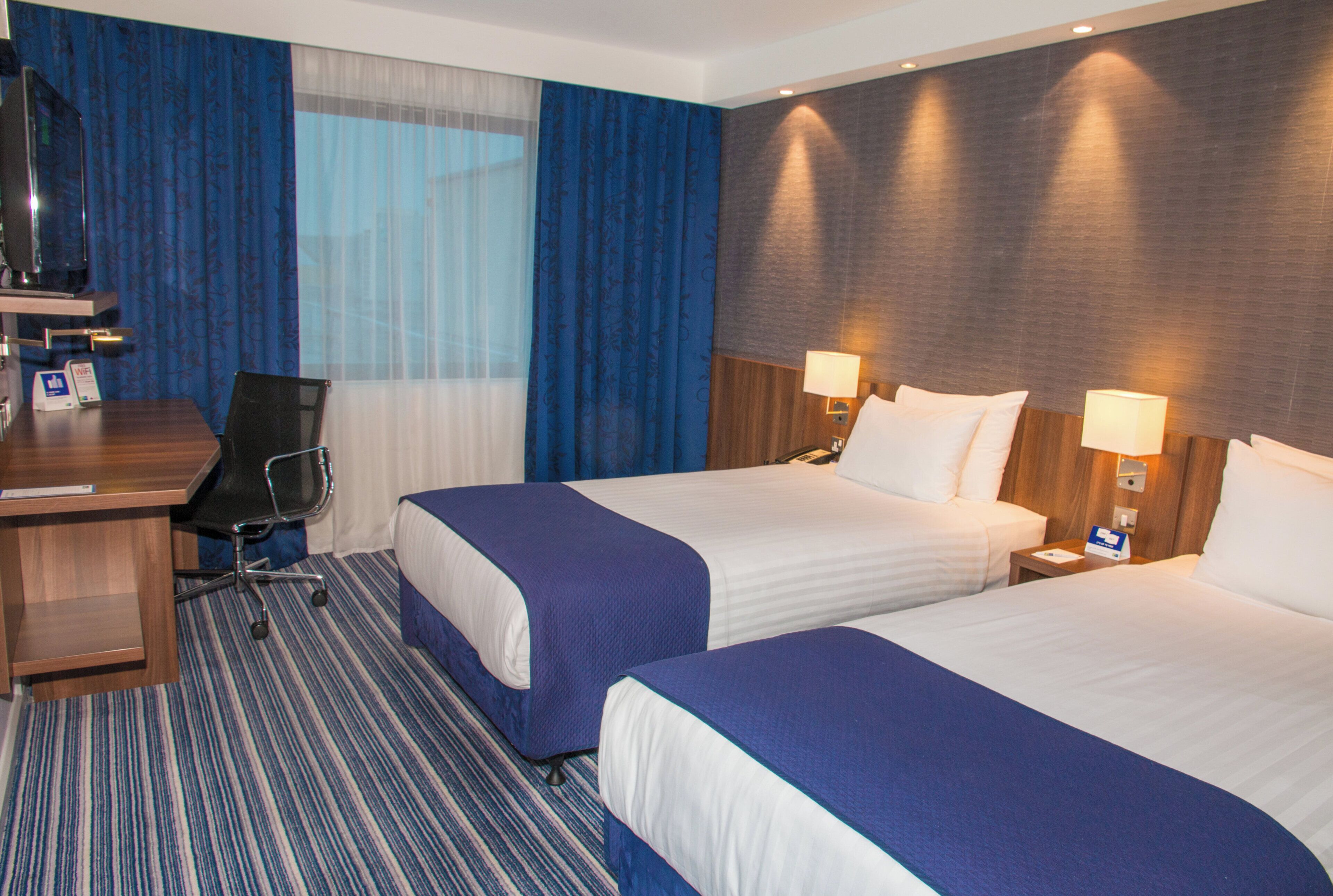 Habitación de hotel con dos camas, un escritorio, una silla y un televisor.