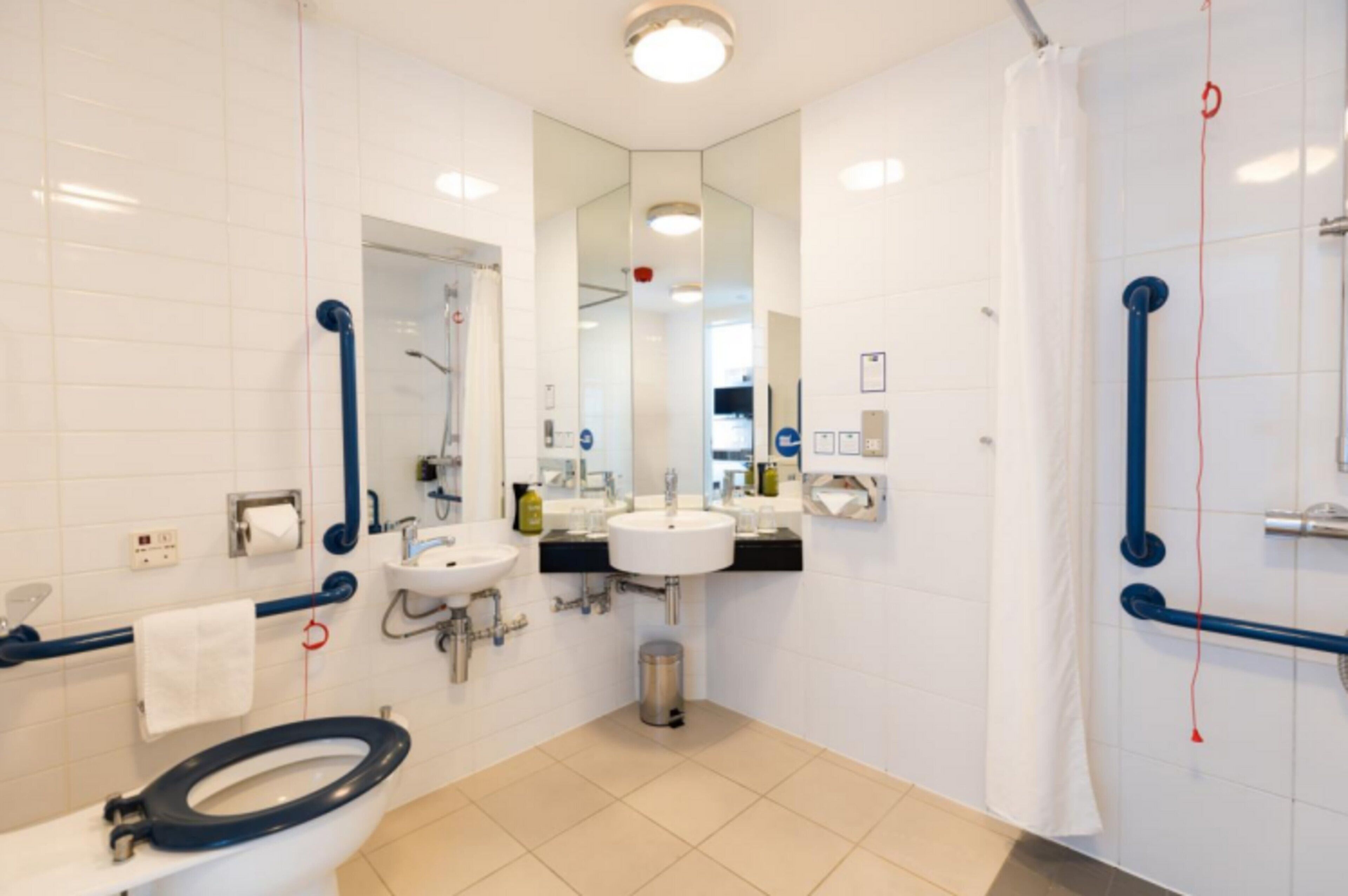 A modern bathroom with white tiles, two sinks, a toilet, and a shower area.