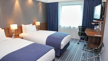 Een hotelkamer met twee bedden, een bureau, een stoel en een groot raam met gordijnen.