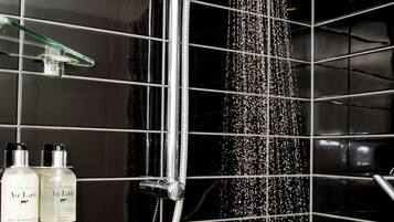 A shower with a rain-like water feature, a glass shelf with bottles, and a black tiled wall.