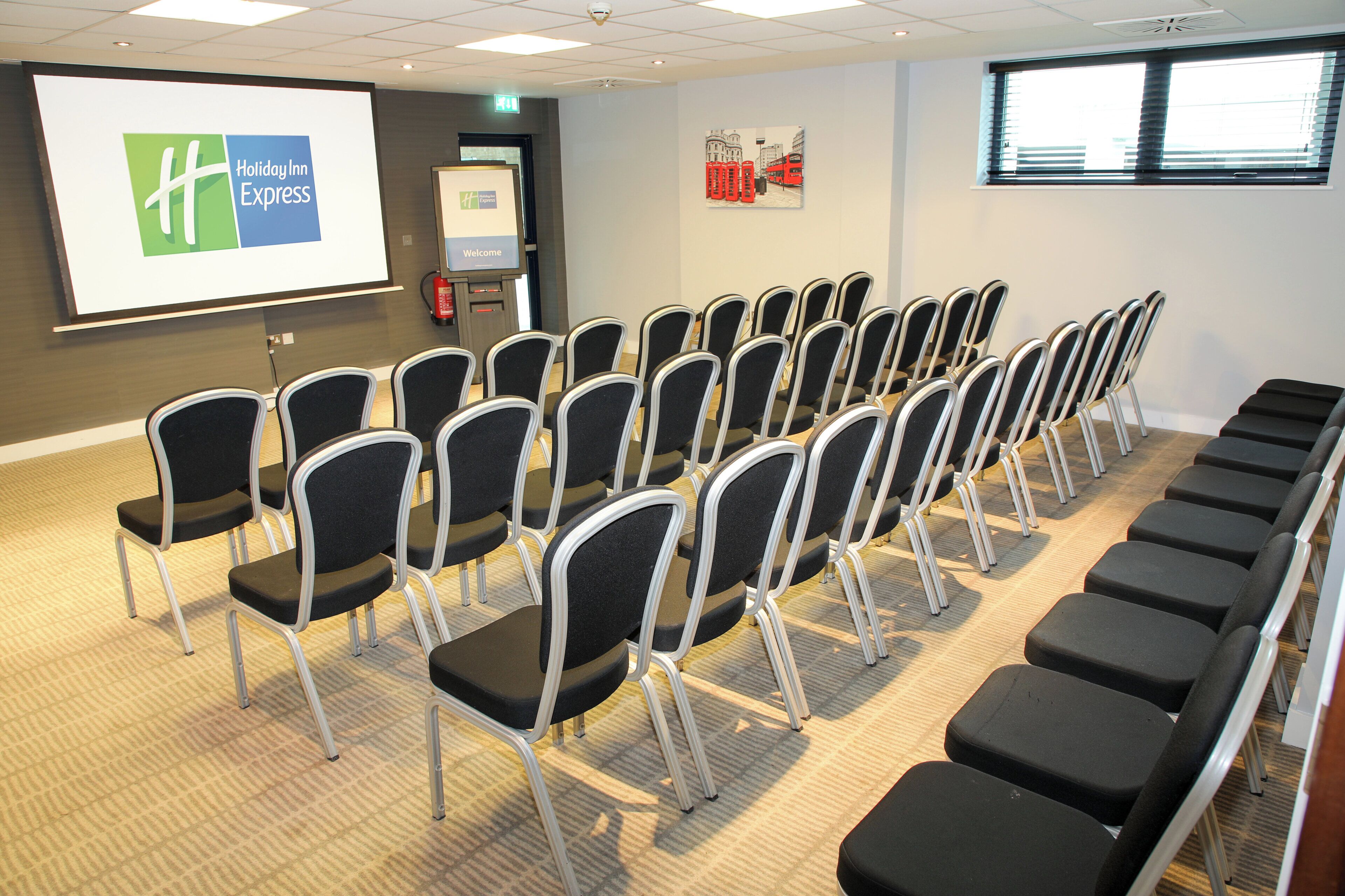 A conference room with rows of chairs, a projector screen displaying a logo, and a welcome sign.