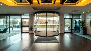 Moderni hotellin aula, jossa on pyörivä ovi, suuret ikkunat ja oleskelualue.
