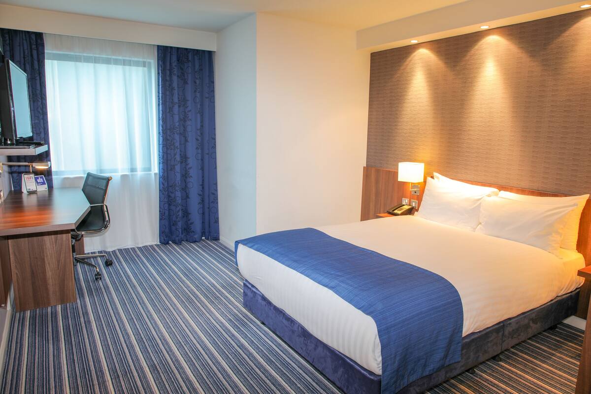 A hotel room with a large bed, a desk, a chair, and a television.