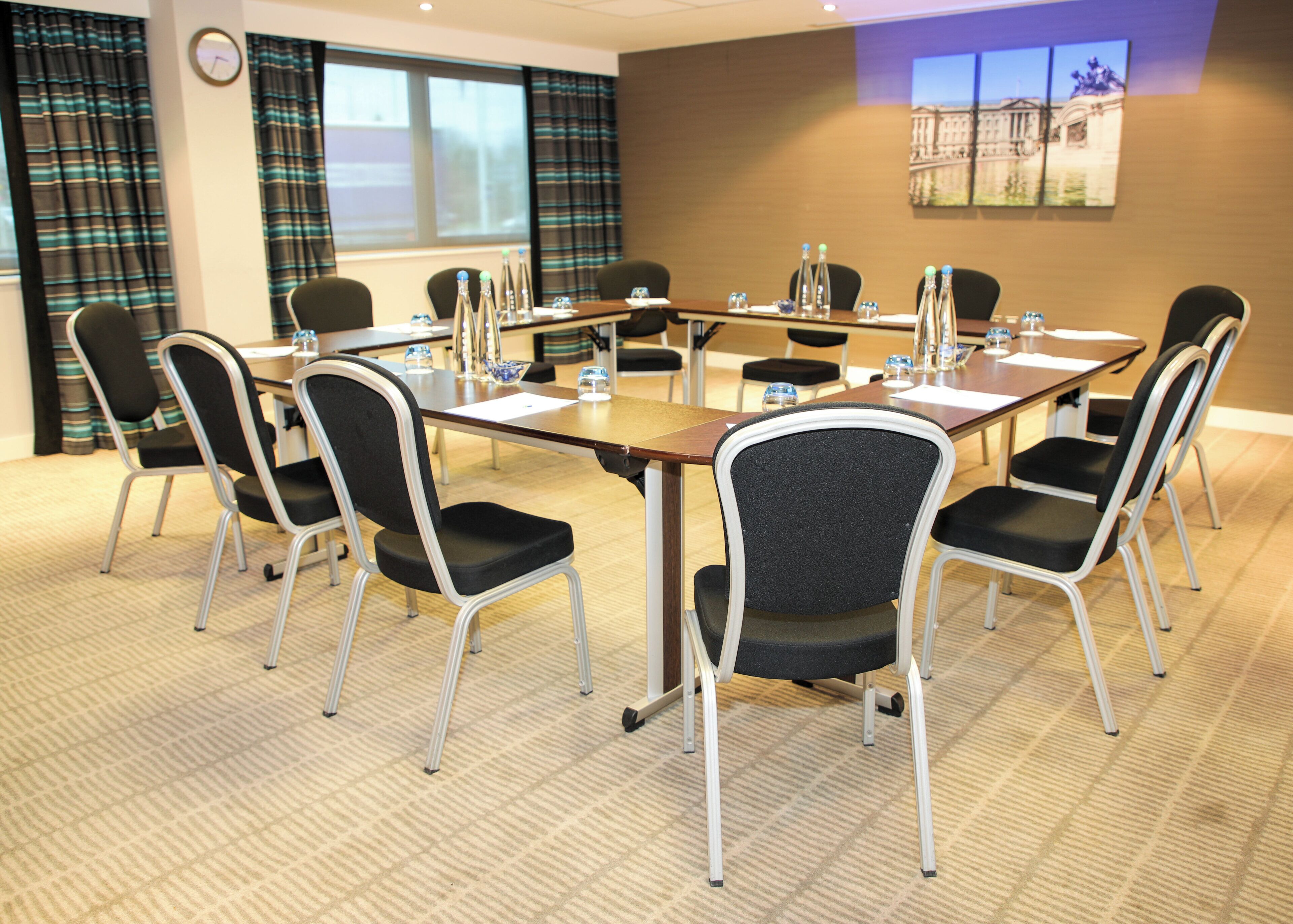 A conference room with a long table, chairs, water bottles, and a clock on the wall.