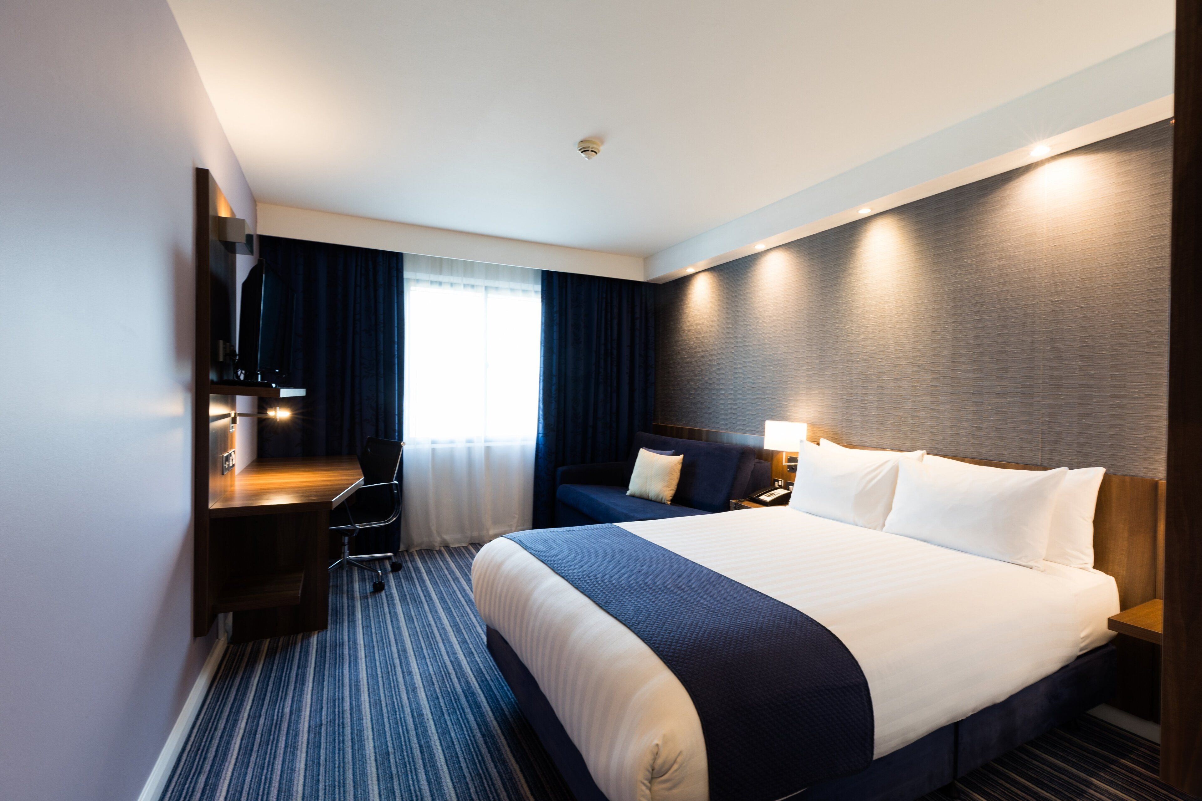 Quarto de hotel moderno com uma cama grande, uma escrivaninha e uma cadeira.