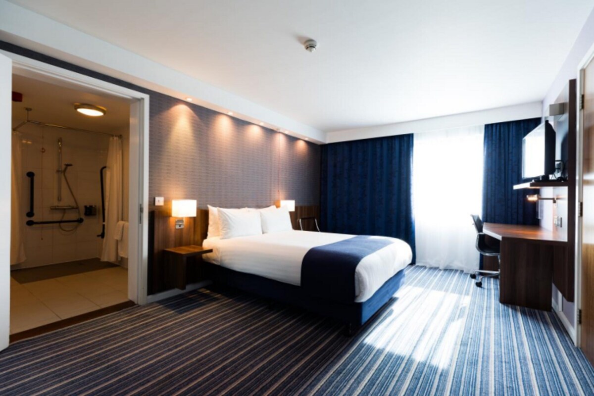 A hotel room with a large bed, bedside tables, a desk, and a shower area.