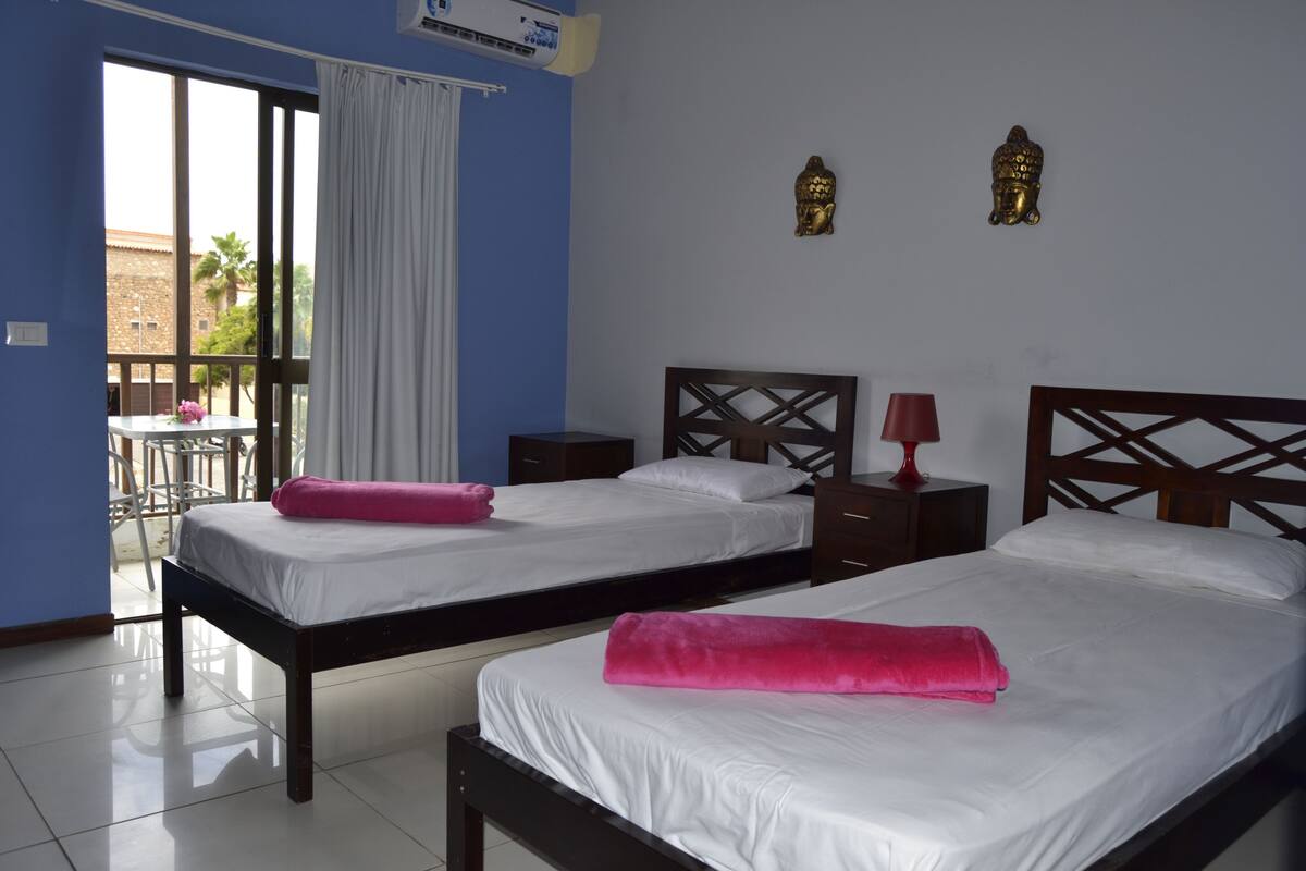 A hotel room with two beds, a balcony, and a view of the outside.