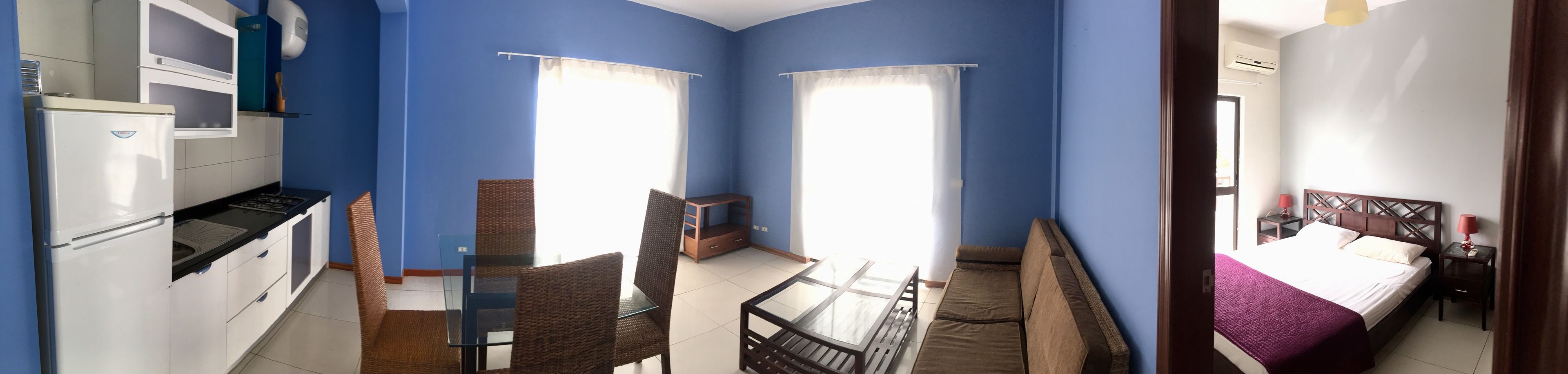 A compact room with a kitchenette, a dining area, and a bed.