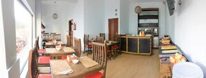 A dining area with multiple tables and chairs, a kitchen area with a counter, and a view of the outside.