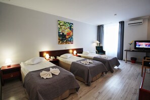 A hotel room with three single beds, a desk with a television, a painting on the wall, and a window with curtains. - A1 Hotel (Riga)