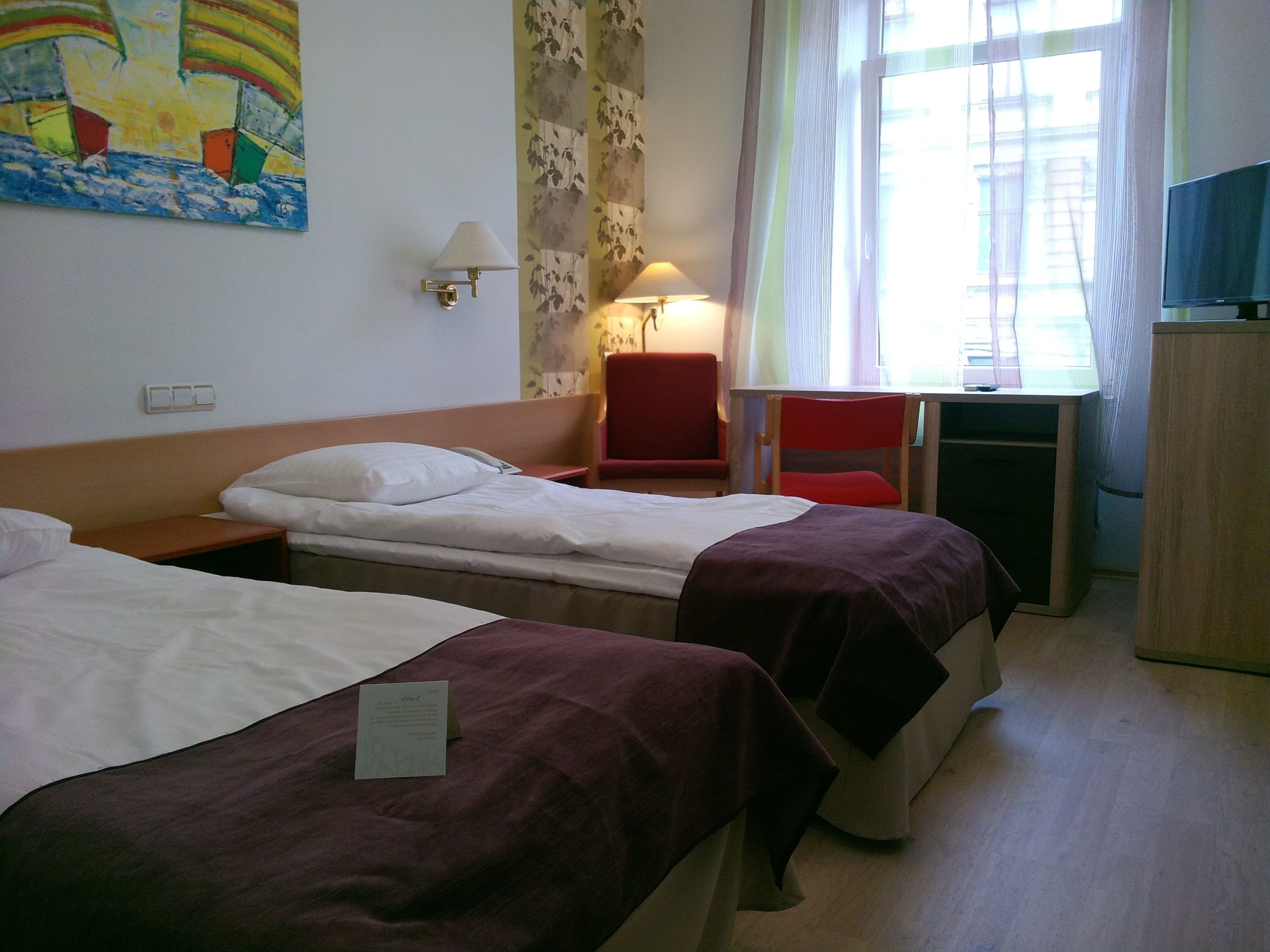 Habitación de hotel con dos camas, un escritorio, una silla, un televisor y un cuadro en la pared.