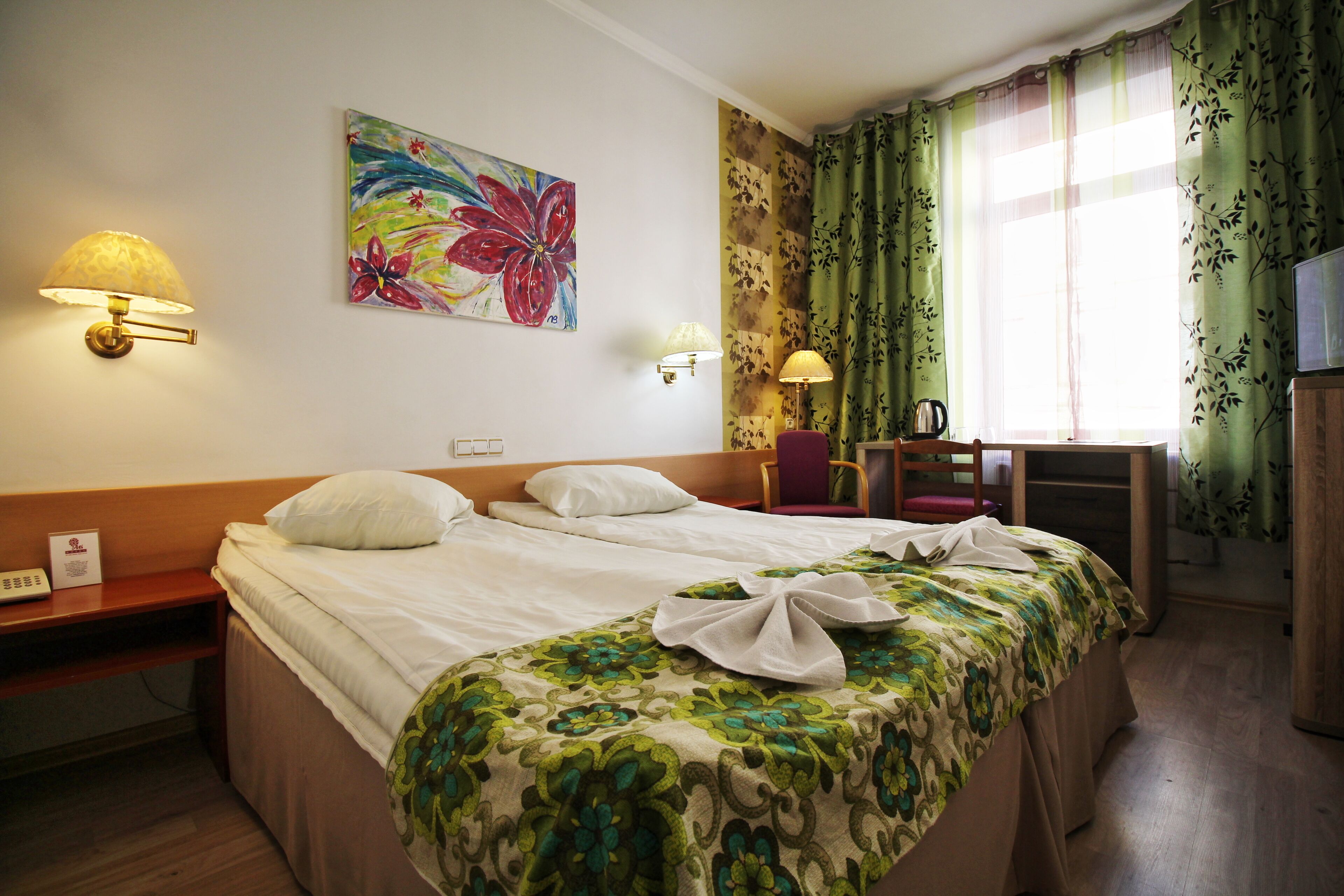 Quarto de hotel com duas camas, uma escrivaninha com cadeira, televisão e um quadro na parede.