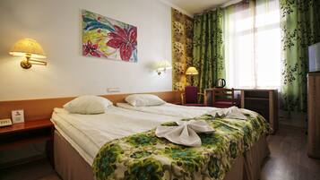 Quarto de hotel com duas camas, uma escrivaninha com cadeira, televisão e um quadro na parede.