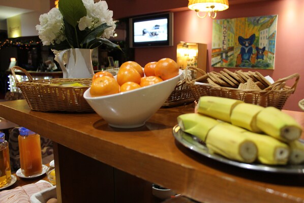 A buffet table with a bowl of oranges, a basket of bread, and a plate of bananas.