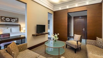 A hotel room with a bed, a TV on a shelf, a glass coffee table, a sofa, and a chair.