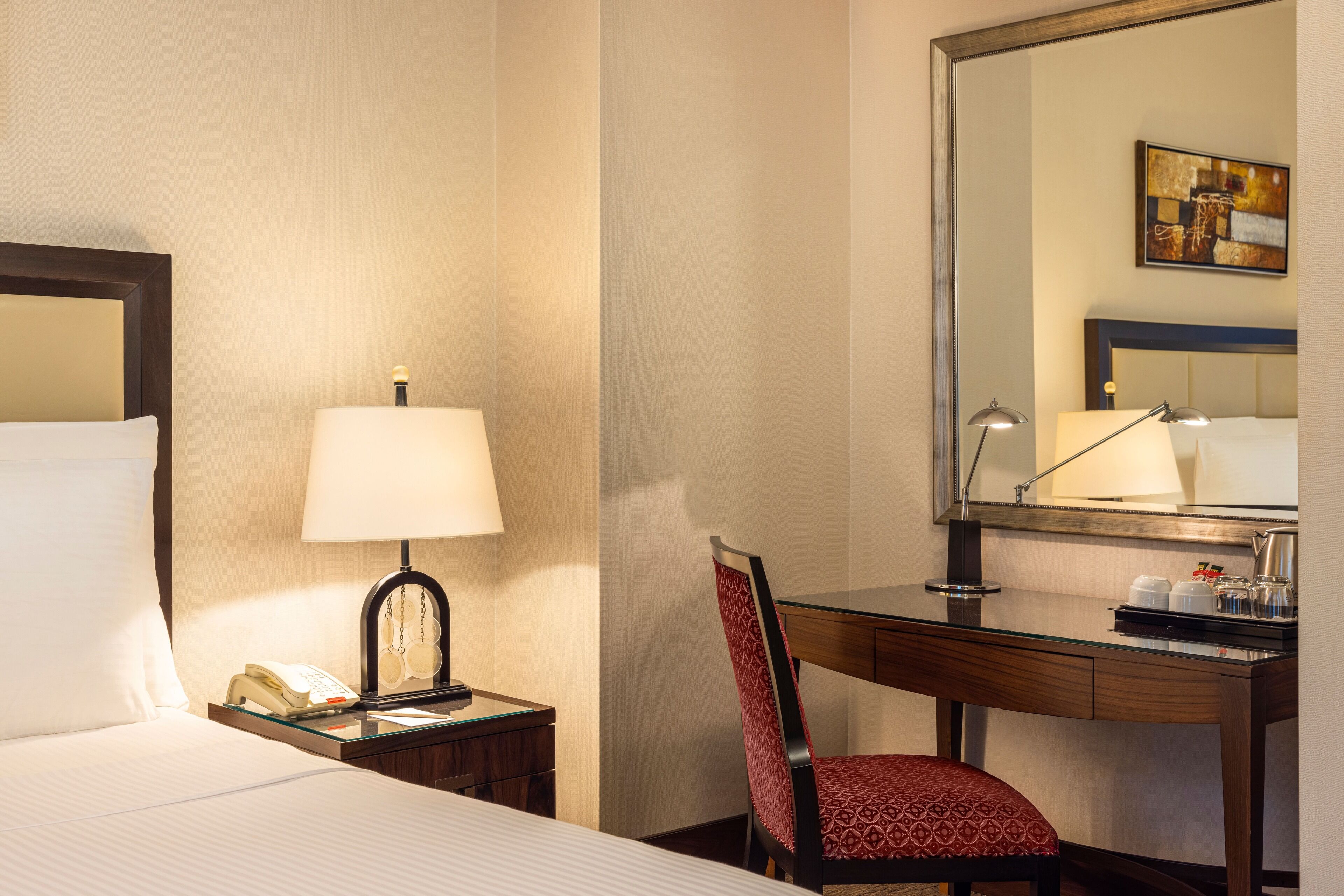Habitación de hotel con cama, mesita de noche con lámpara, escritorio con silla y un espejo grande.
