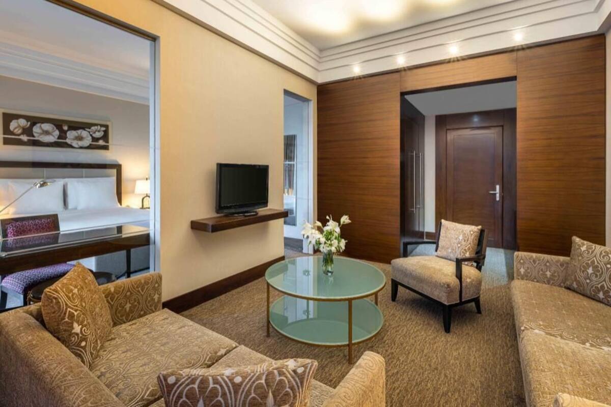 A hotel room with a sofa set, a glass coffee table, a TV, and a wooden door.
