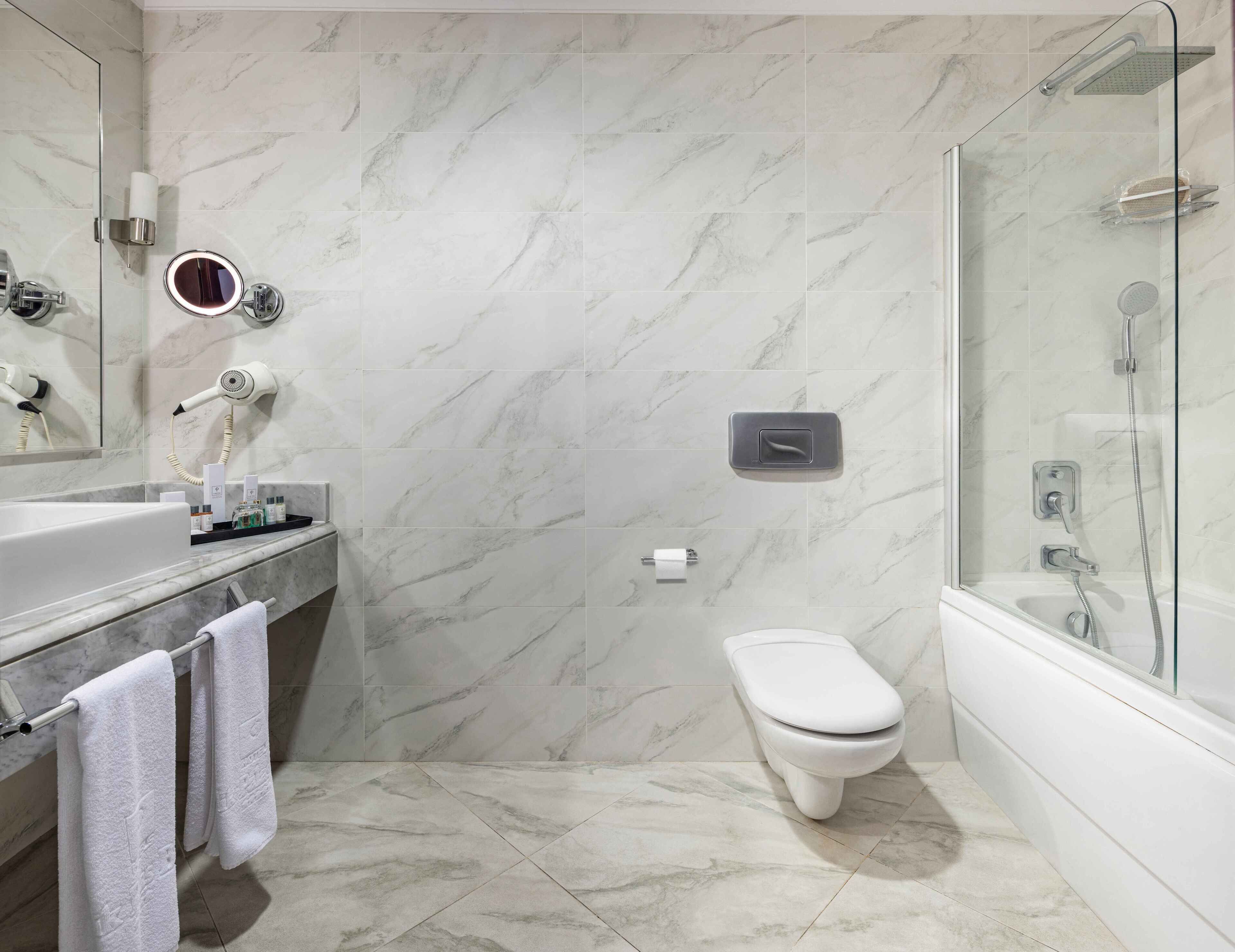 A modern bathroom with a marble floor, a glass shower enclosure, a toilet, and a vanity with a mirror and towel rack.