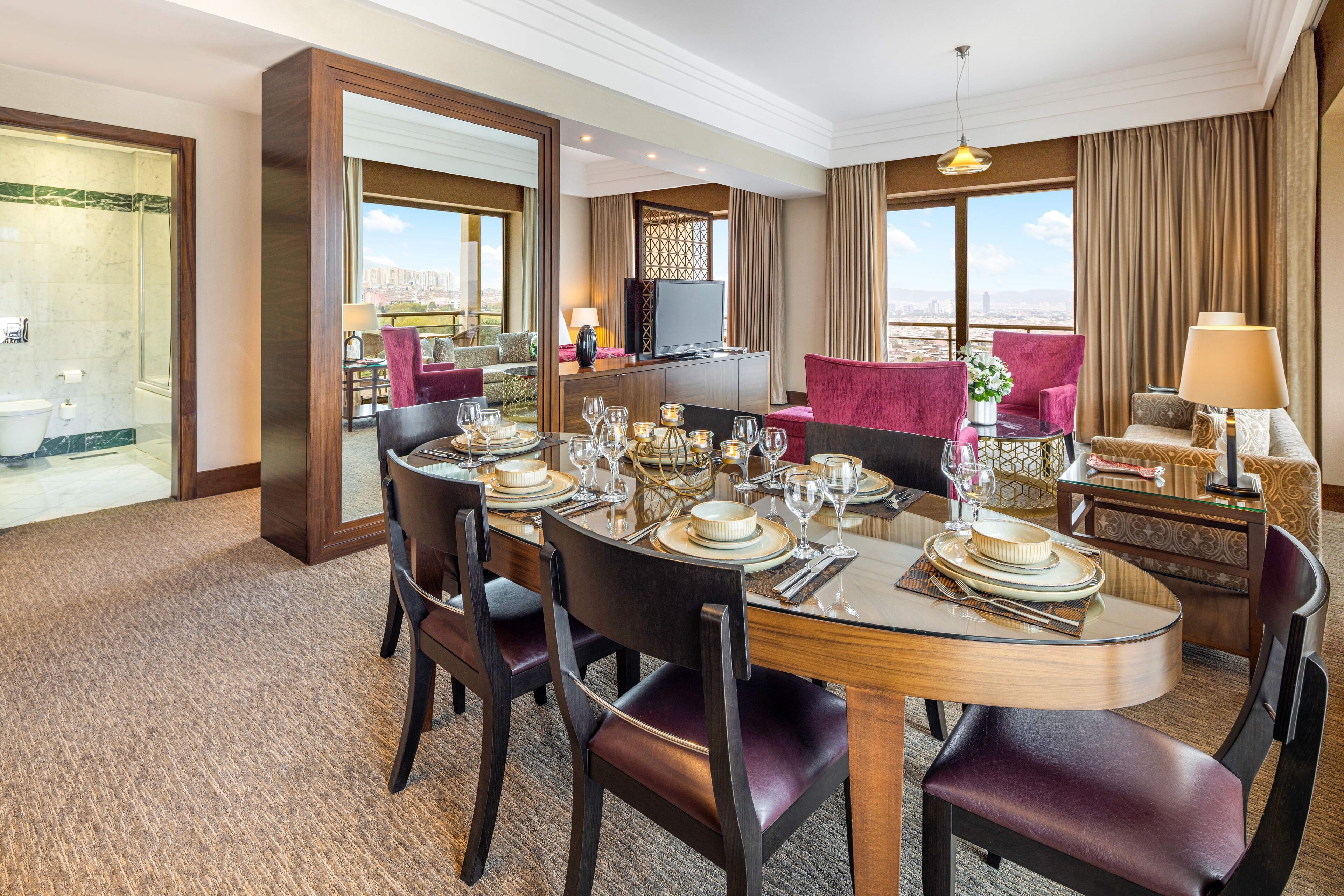 Habitación de hotel con comedor listo para una comida, televisor y vista a la ciudad.